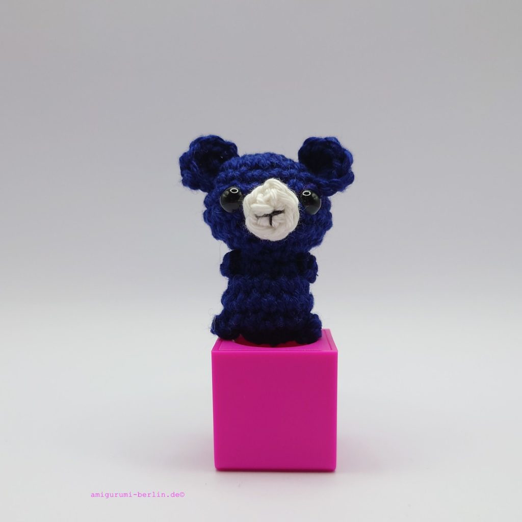ein marineblauer gehäkelter Bär auf einem pinkfarbenen Block - a navy-blue crocheted bear on a pink block