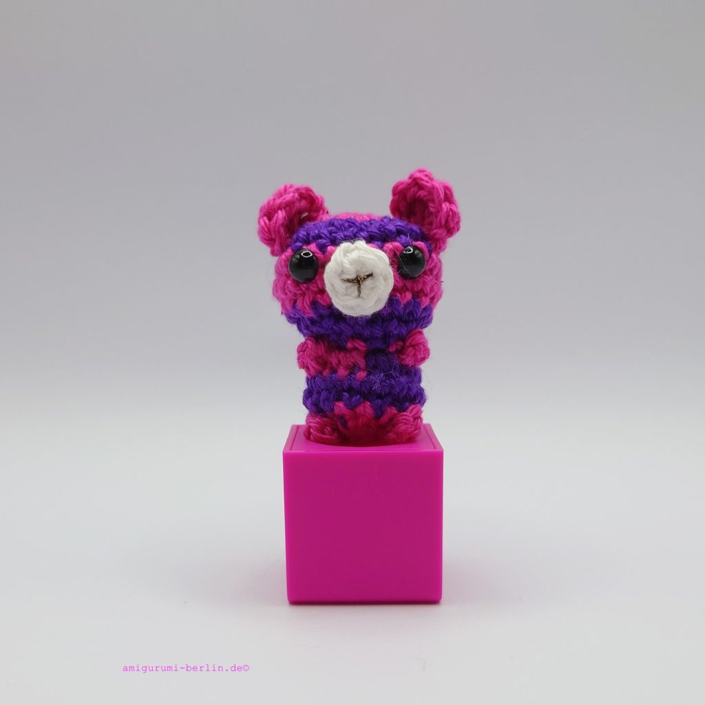 ein violett-pinkfarbener gehäkelter Bär auf einem pinkfarbenen Block - a purple-pink-coloured crocheted bear on a pink block