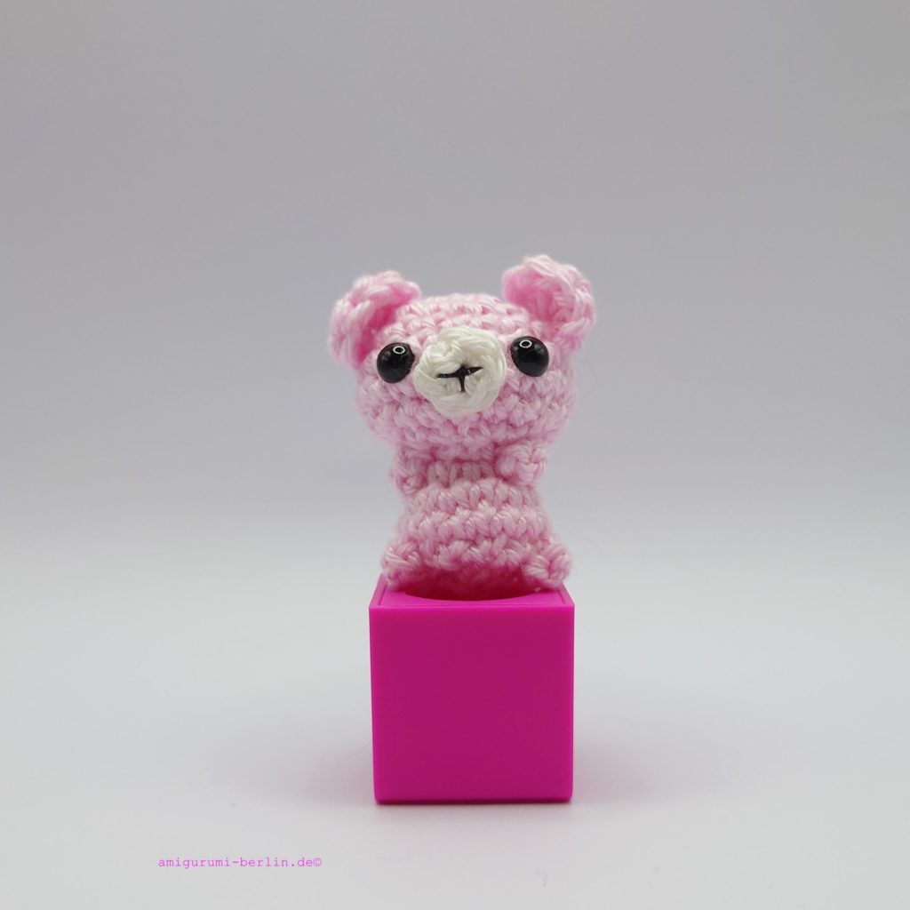 ein rosafarbener gehäkelter Bär auf einem pinkfarbenen Block - a pink-coloured crocheted bear on a pink block
