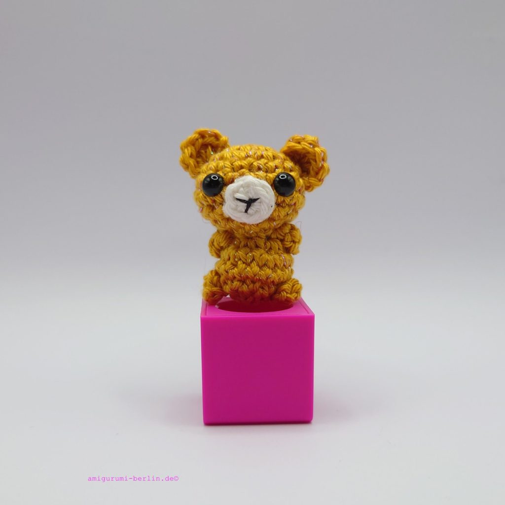 ein goldfarbener gehäkelter Bär auf einem pinkfarbenen Block - a gold-coloured crocheted bear on a pink block