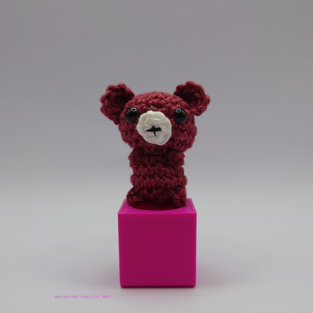 ein bordeauxfarbener gehäkelter Bär auf einem pinkfarbenen Block - a burgundy-coloured crocheted bear on a pink block