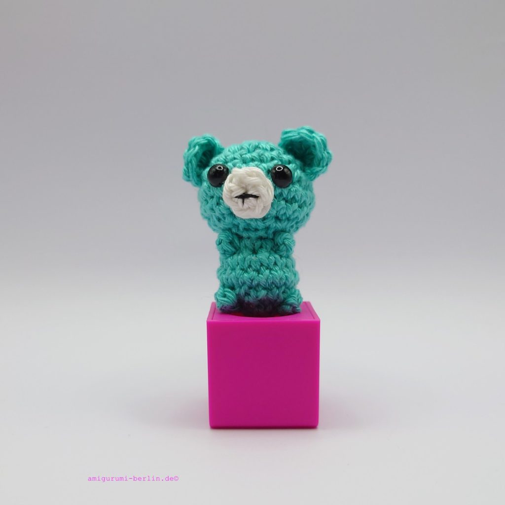 ein jadefarbener gehäkelter Bär auf einem pinkfarbenen Block - a jade-coloured crocheted bear on a pink block