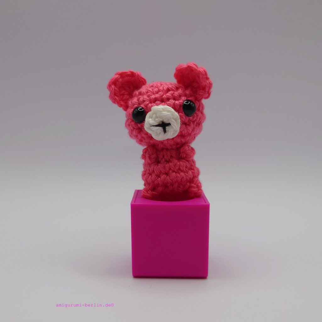 ein himbeerfarbener gehäkelter Bär auf einem pinkfarbenen Block - a raspberry-coloured crocheted bear on a pink block