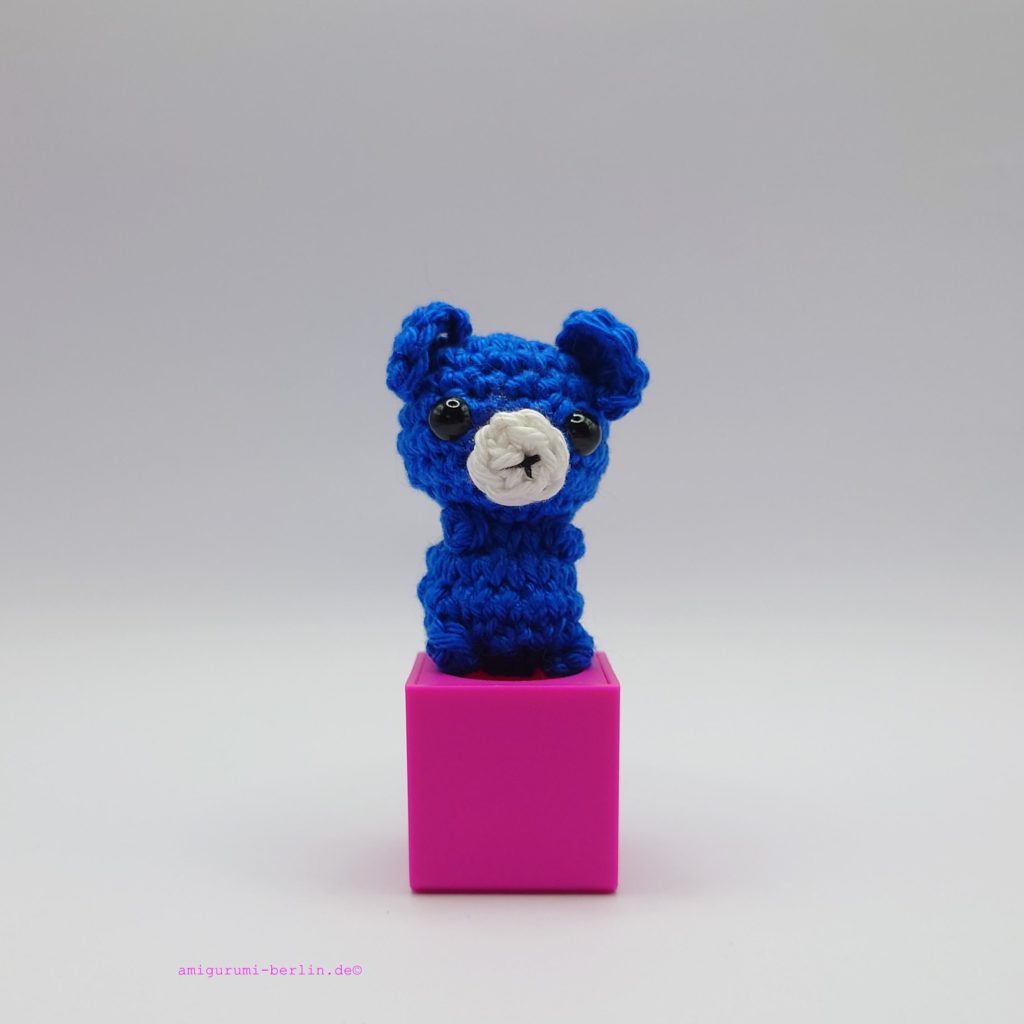 ein royalblauer gehäkelter Bär auf einem pinkfarbenen Block - a royal-blue crocheted bear on a pink block
