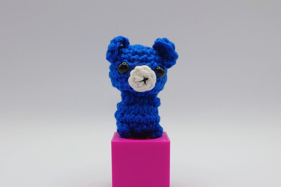 ein royalblauer gehäkelter Bär auf einem pinkfarbenen Block - a royal-blue crocheted bear on a pink block