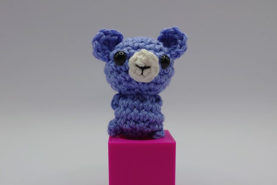 ein wolkefarbener gehäkelter Bär auf einem pinkfarbenen Block - a cloud-coloured crocheted bear on a pink block