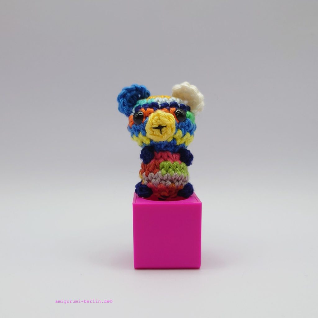 ein restebunter gehäkelter Bär auf einem pinkfarbenen Block - a -colorful crocheted bear on a pink block