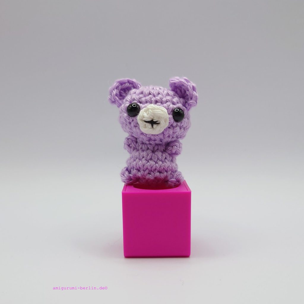 ein lavendelfarbener gehäkelter Bär auf einem pinkfarbenen Block - a lavender-coloured crocheted bear on a pink block