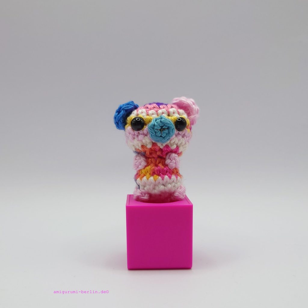 ein bunter gehäkelter Bär auf einem pinkfarbenen Block - a colourful crocheted bear on a pink block