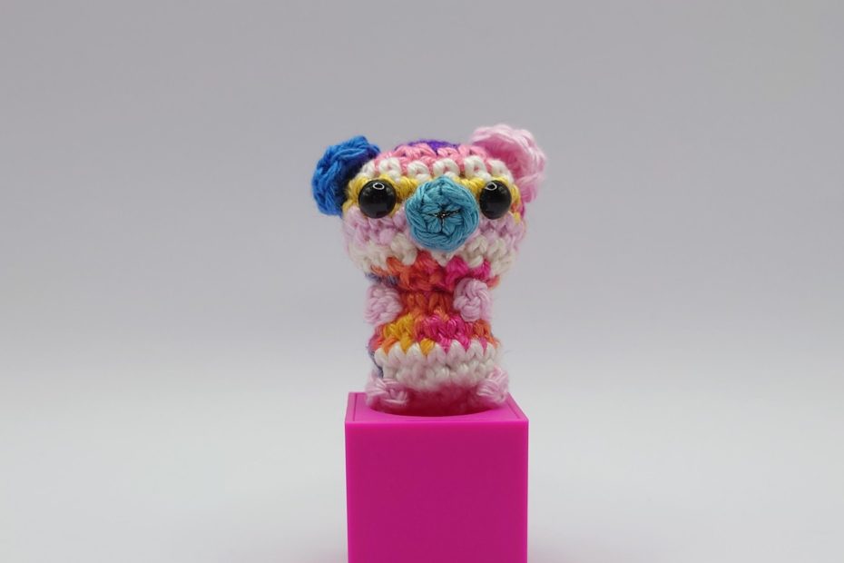 ein bunter gehäkelter Bär auf einem pinkfarbenen Block - a colourful crocheted bear on a pink block