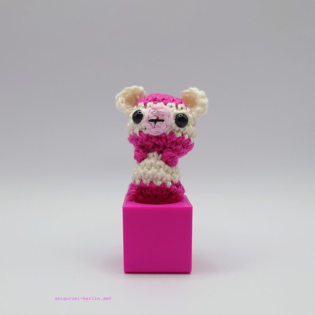 ein weiß-pinkfarbener gehäkelter Bär auf einem pinkfarbenen Block - a white-pink-coloured crocheted bear on a pink block