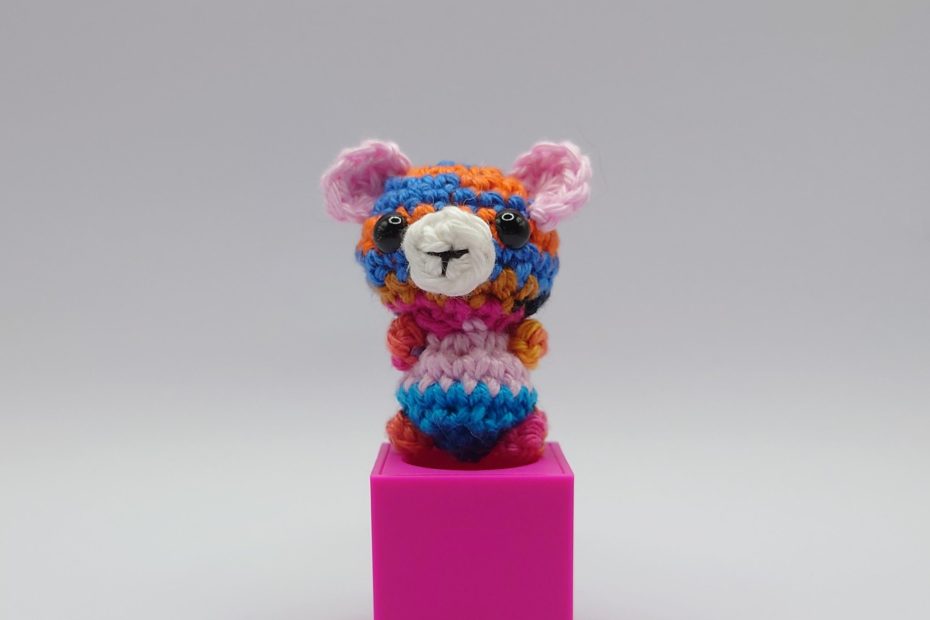 ein bunter gehäkelter Bär auf einem pinkfarbenen Block - a colourful crocheted bear on a pink block