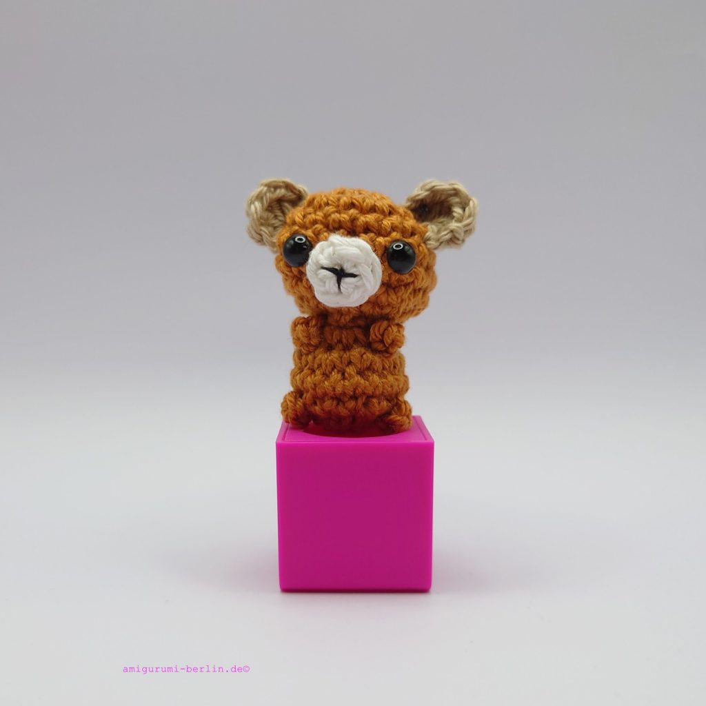 ein maronefarbener gehäkelter Bär auf einem pinkfarbenen Block - a chestnut-coloured crocheted bear on a pink block
