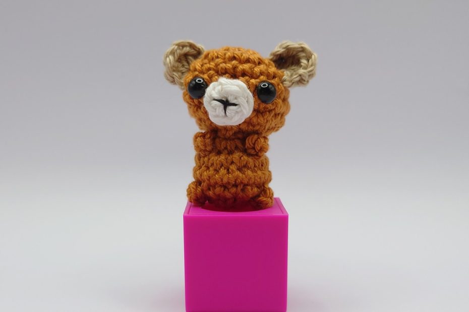 ein maronefarbener gehäkelter Bär auf einem pinkfarbenen Block - a chestnut-coloured crocheted bear on a pink block