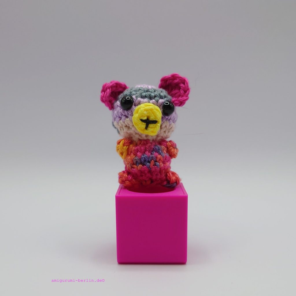 ein bunter gehäkelter Bär auf einem pinkfarbenen Block - a colourful crocheted bear on a pink block