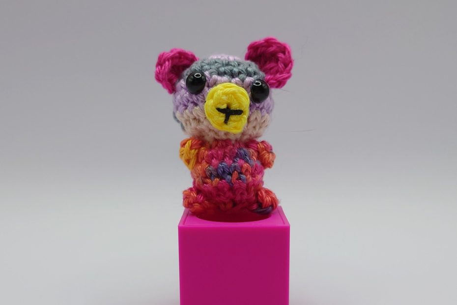 ein bunter gehäkelter Bär auf einem pinkfarbenen Block - a colourful crocheted bear on a pink block