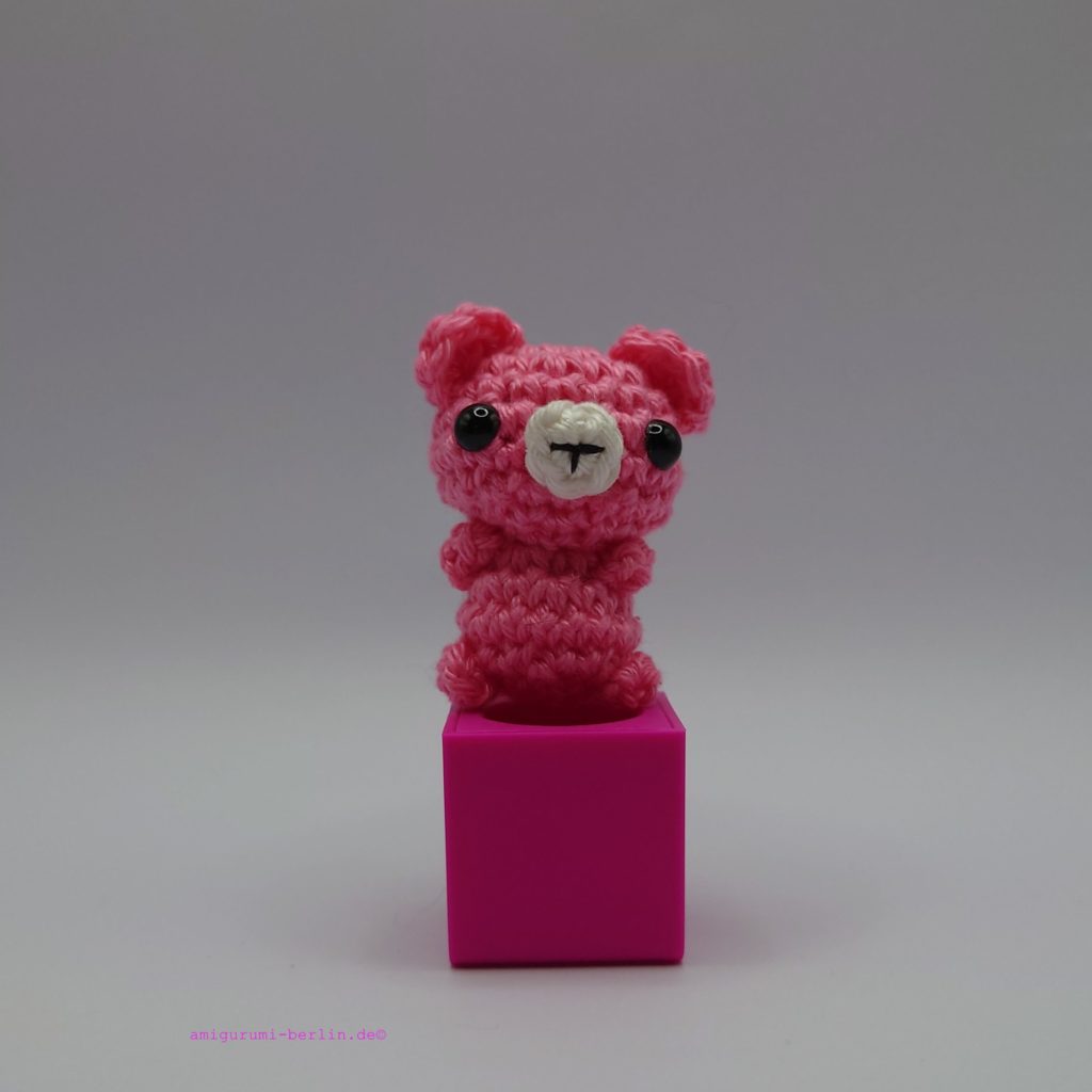 ein orchideefarbener gehäkelter Bär auf einem pinkfarbenen Block - a orchid-coloured crocheted bear on a pink block