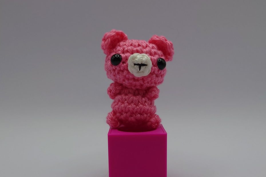 ein orchideefarbener gehäkelter Bär auf einem pinkfarbenen Block - a orchid-coloured crocheted bear on a pink block