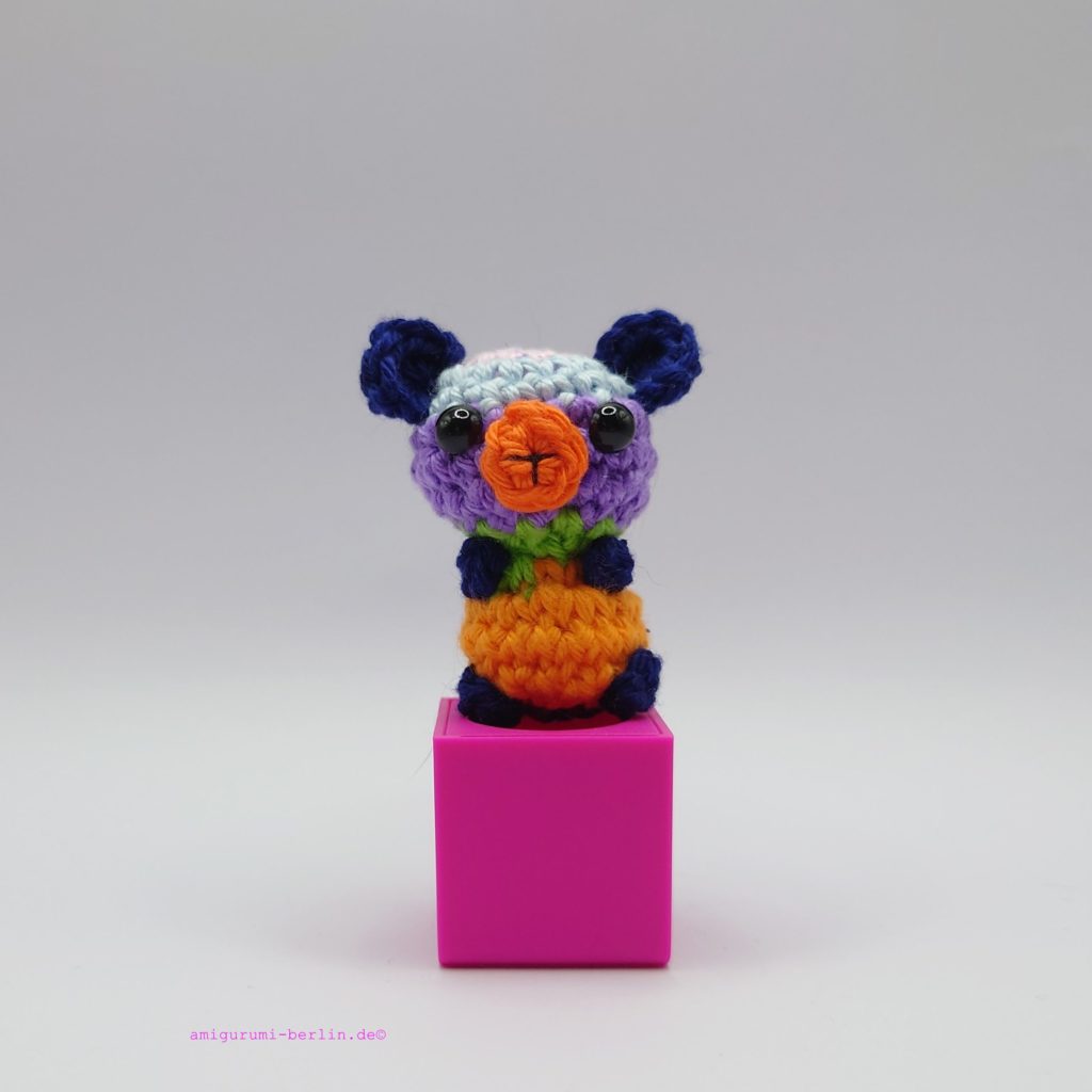 ein bunter gehäkelter Bär auf einem pinkfarbenen Block - a colourful crocheted bear on a pink block