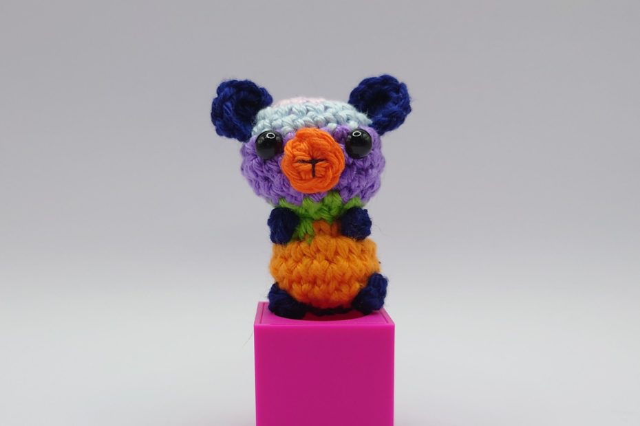 ein bunter gehäkelter Bär auf einem pinkfarbenen Block - a colourful crocheted bear on a pink block