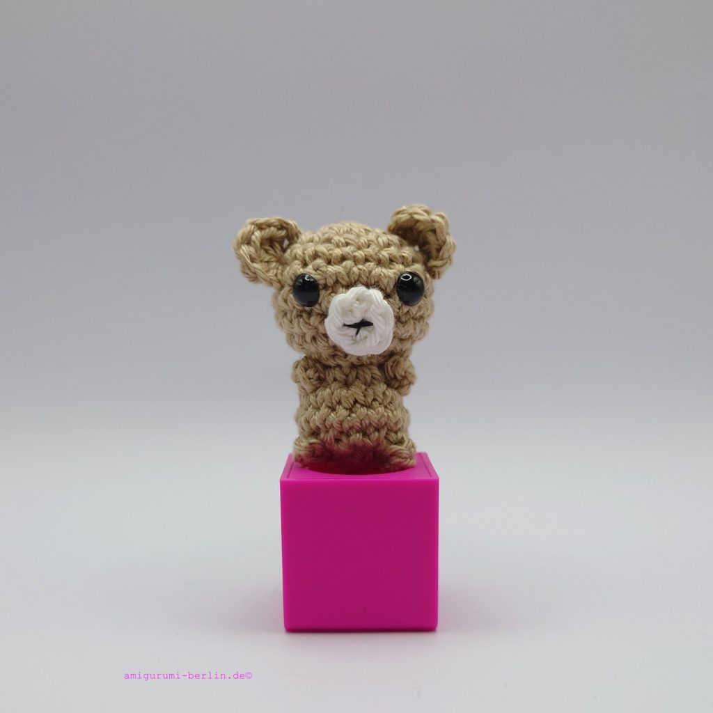 ein leinenfarbener gehäkelter Bär auf einem pinkfarbenen Block - a linen-coloured crocheted bear on a pink block