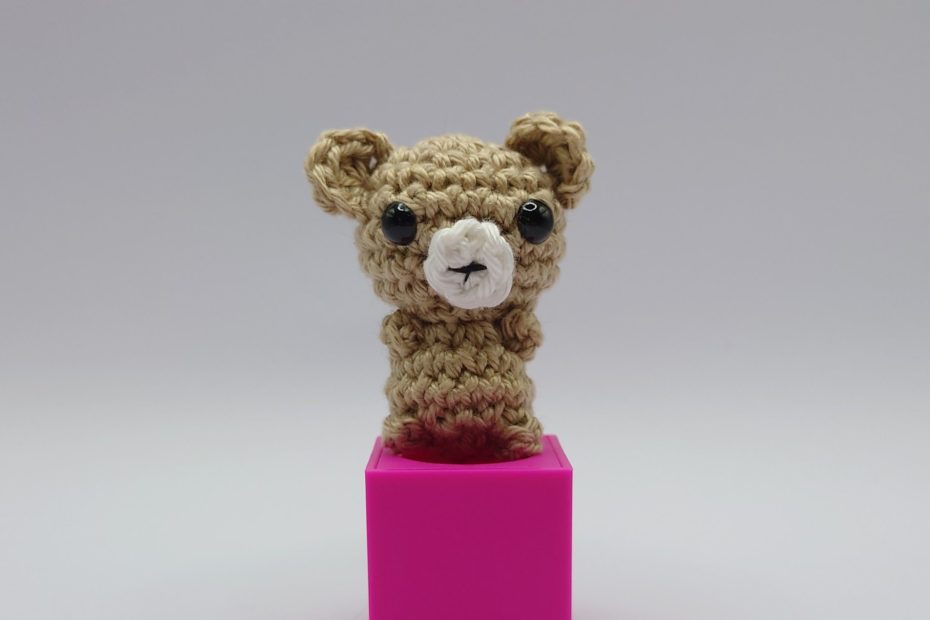 ein leinenfarbener gehäkelter Bär auf einem pinkfarbenen Block - a linen-coloured crocheted bear on a pink block