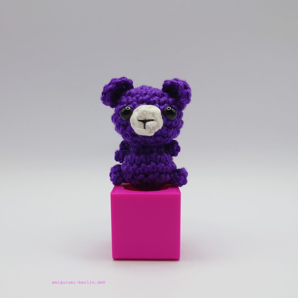 ein violetter gehäkelter Bär auf einem pinkfarbenen Block - a purple crocheted bear on a pink block