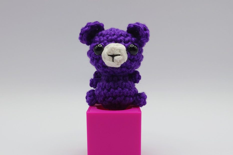 ein violetter gehäkelter Bär auf einem pinkfarbenen Block - a purple crocheted bear on a pink block