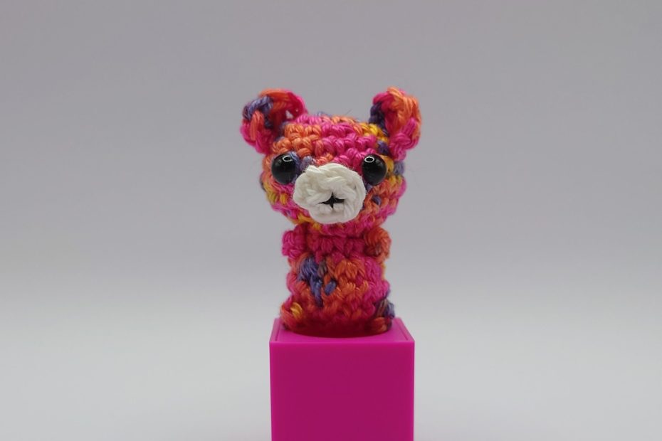 ein bunter gehäkelter Bär auf einem pinkfarbenen Block - a colourful crocheted bear on a pink block