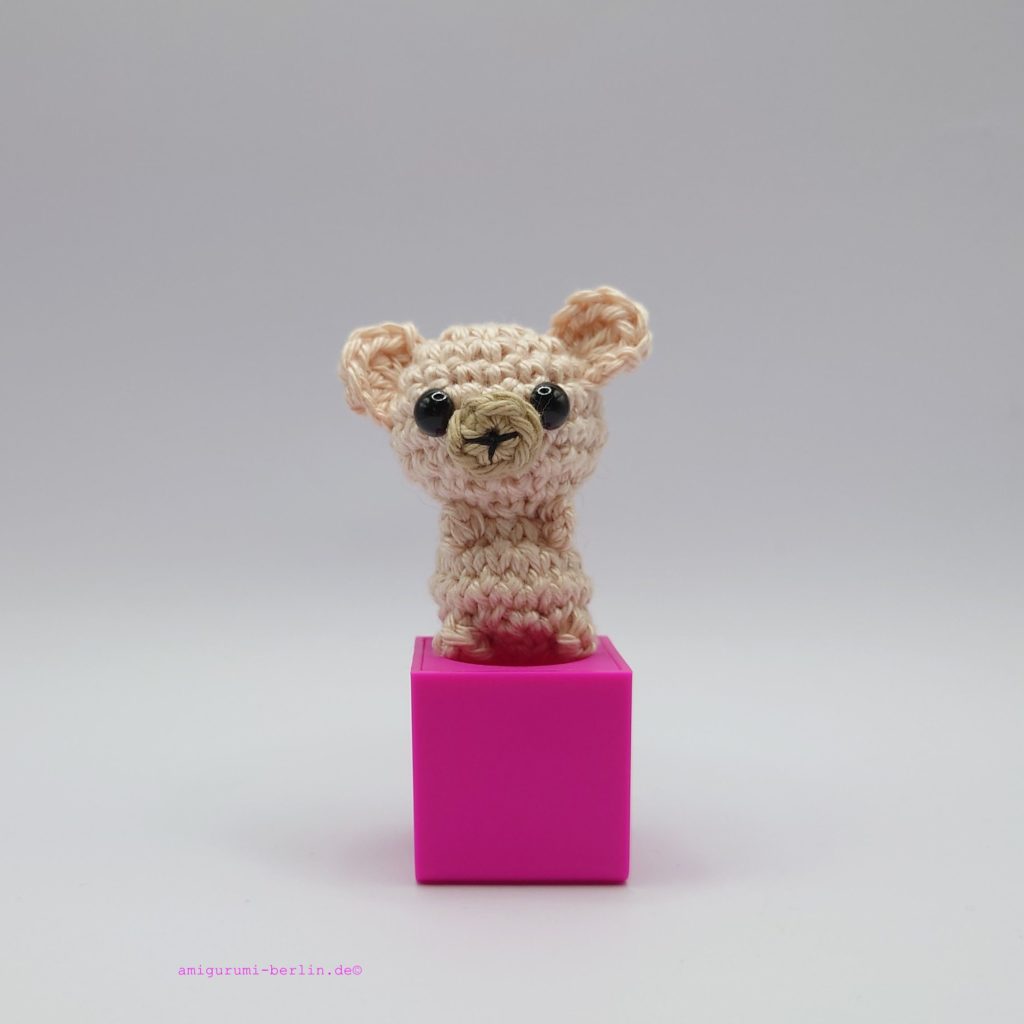 ein naturfarbener gehäkelter Bär auf einem pinkfarbenen Block a nature-coloured crocheted bear on a pink block
