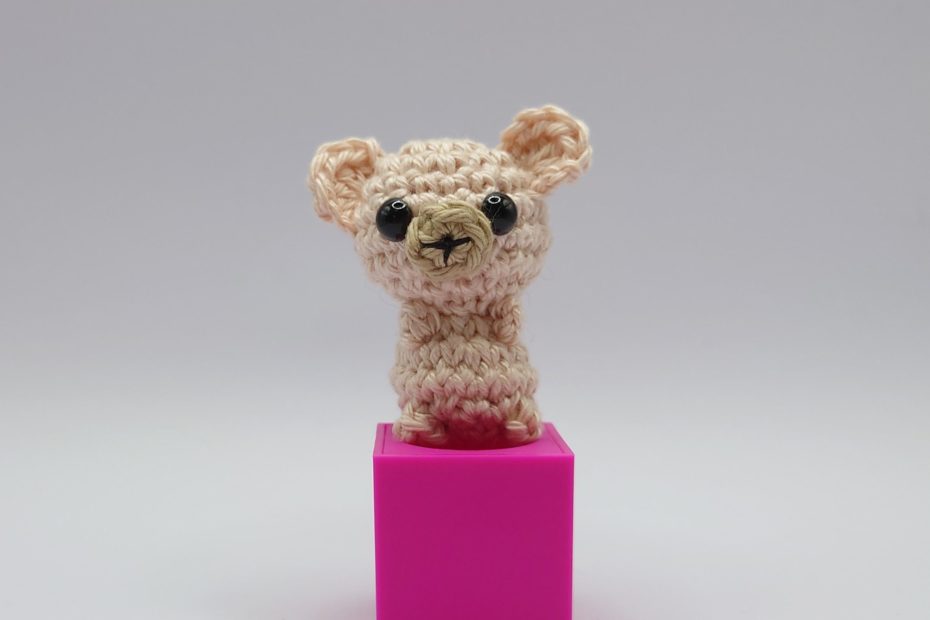 ein naturfarbener gehäkelter Bär auf einem pinkfarbenen Block a nature-coloured crocheted bear on a pink block