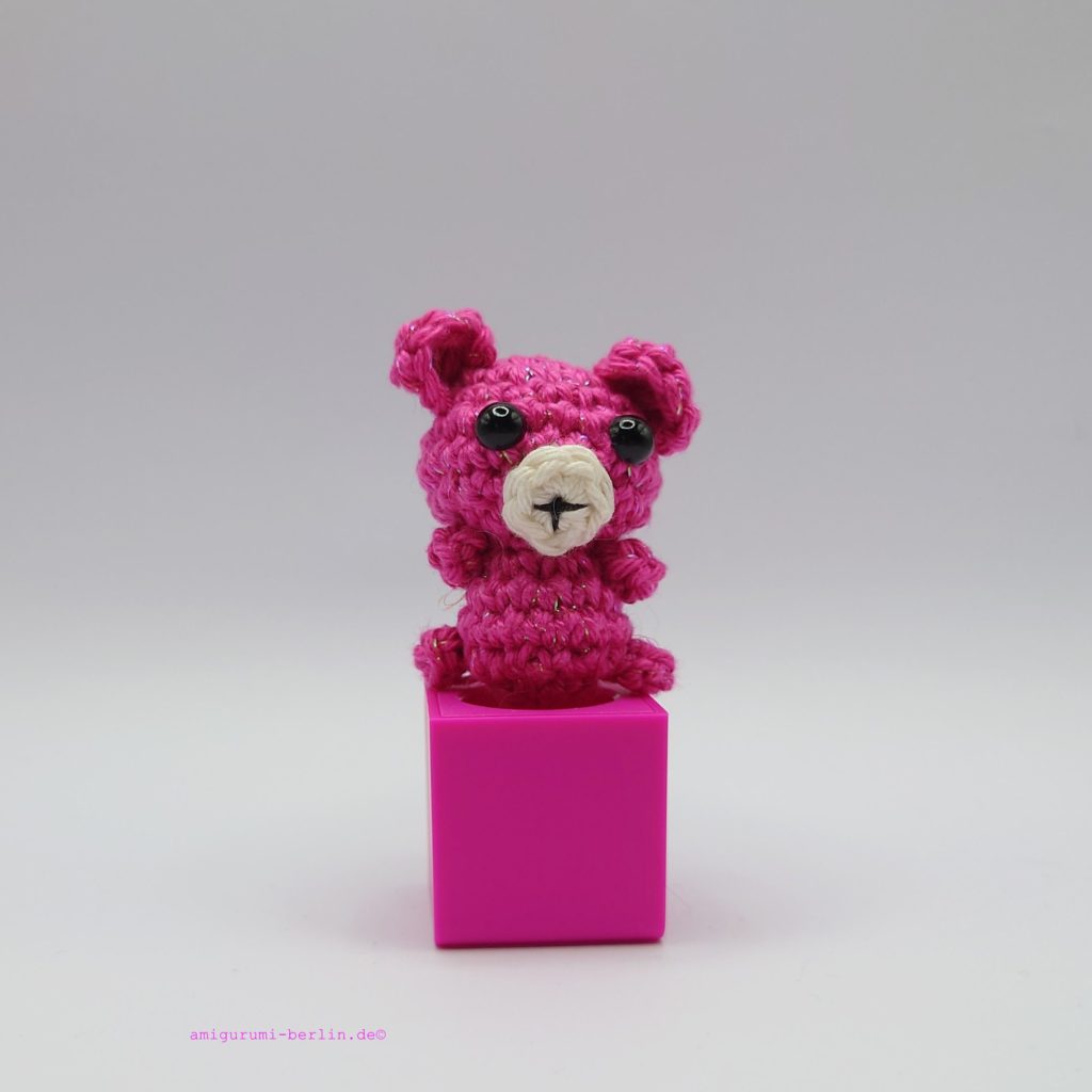 ein cyclamfarbener gehäkelter Bär auf einem pinkfarbenen Block a cyclam-coloured crocheted bear on a pink block