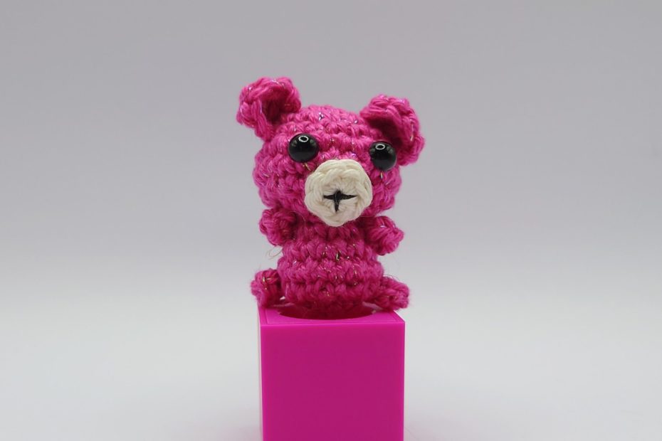 ein cyclamfarbener gehäkelter Bär auf einem pinkfarbenen Block a cyclam-coloured crocheted bear on a pink block
