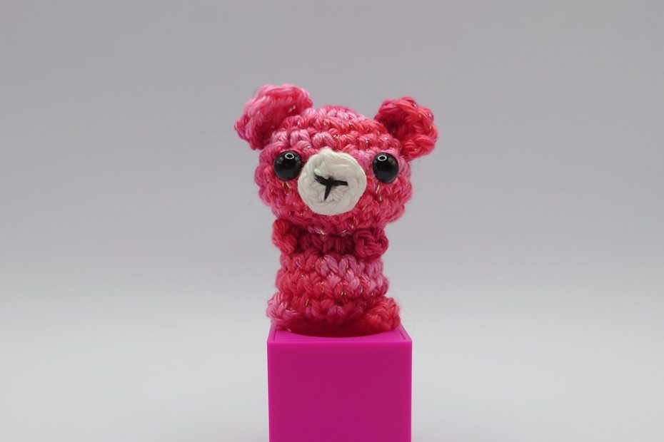ein him- und erdbeerfarbener gehäkelter Bär auf einem pinkfarbenen Block a raspberry and strawberry-coloured crocheted bear on a pink block
