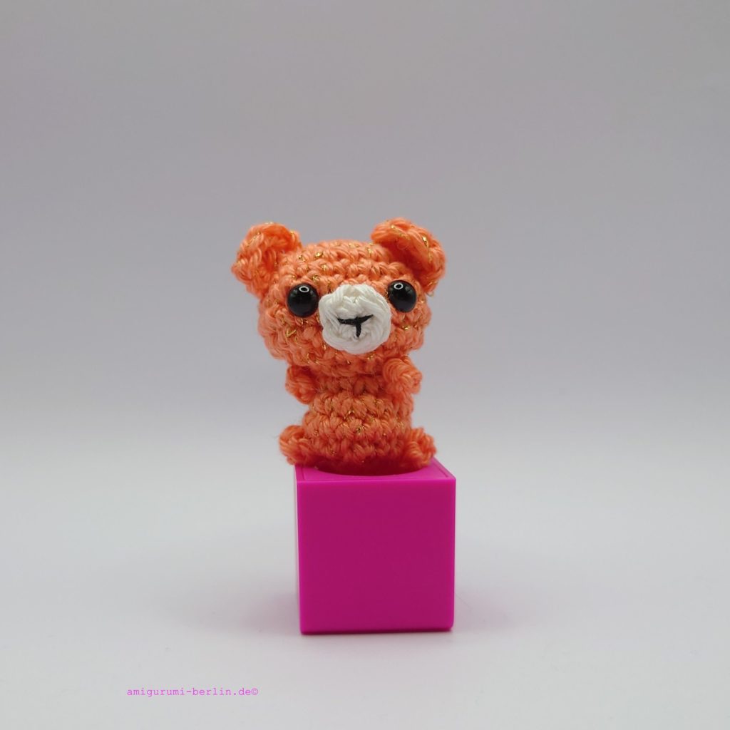 ein korallefarbener gehäkelter Bär auf einem pinkfarbenen Block a coral-coloured crocheted bear on a pink block