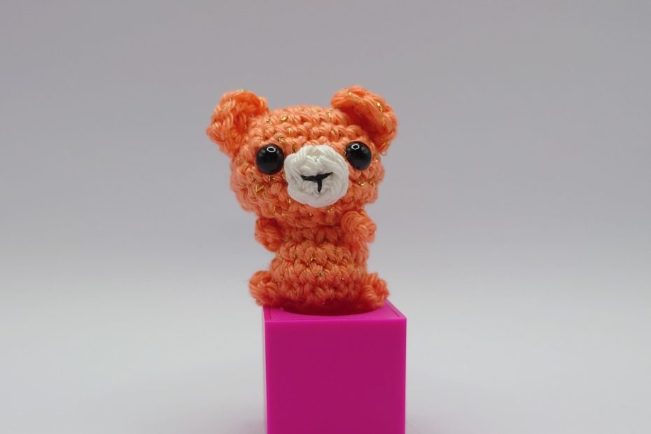 ein korallefarbener gehäkelter Bär auf einem pinkfarbenen Block a coral-coloured crocheted bear on a pink block